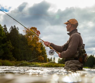A man casts his fly rod into a river during the autumnA man casts his fly rod into a river during the autumn